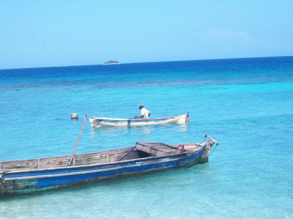 Fisherman in a small boat on turquoise Caribbean waters with a wooden boat in the foreground