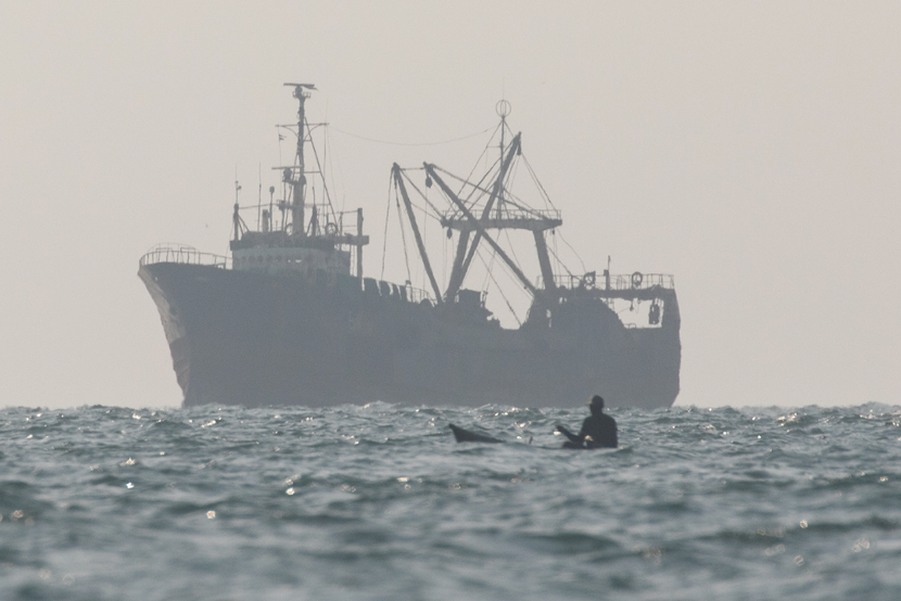 Small-scale fisherman in a canoe near a large industrial fishing trawler at sea