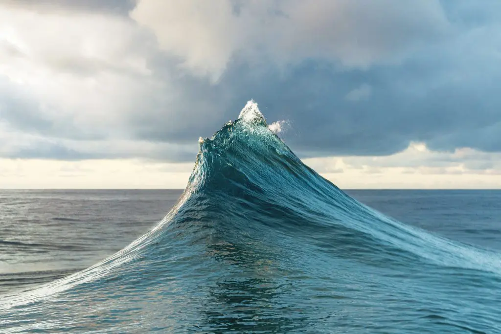 A large ocean wave cresting against a cloudy sky.