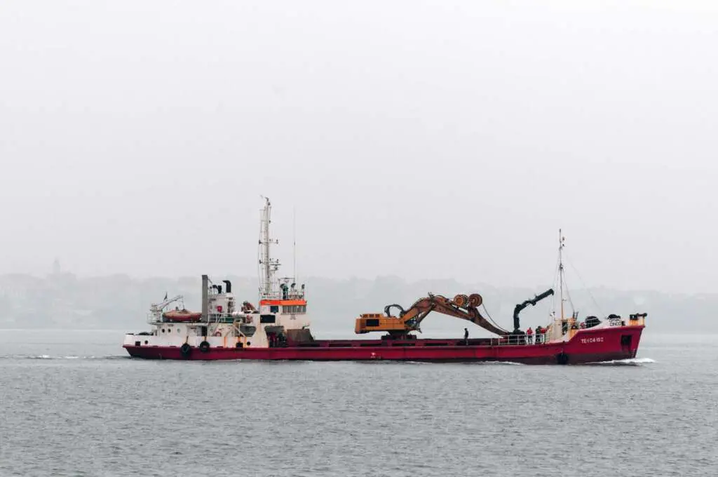 Red dredging vessel with a crane at sea on a foggy day