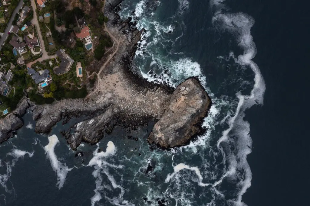 Aerial view of a rocky coastline with waves and coastal properties at Zapallar