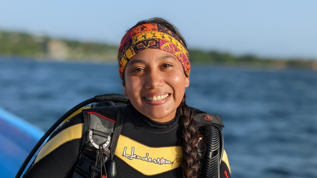 A young woman in scuba gear smiling aboard a boat.