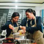 Several women in aprons cooking together at a table with pots and pans.