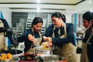 Several women in aprons cooking together at a table with pots and pans.