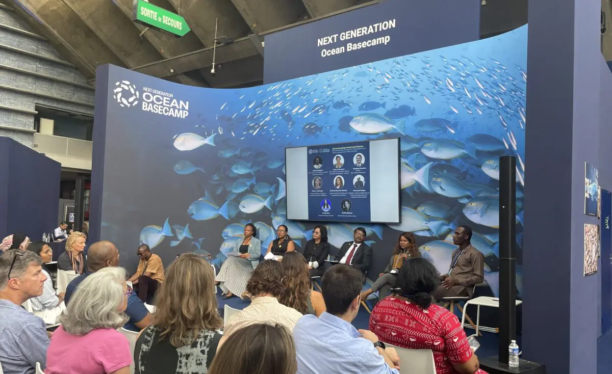 Panellists seated on stage addressing an audience in front of an underwater-themed backdrop.