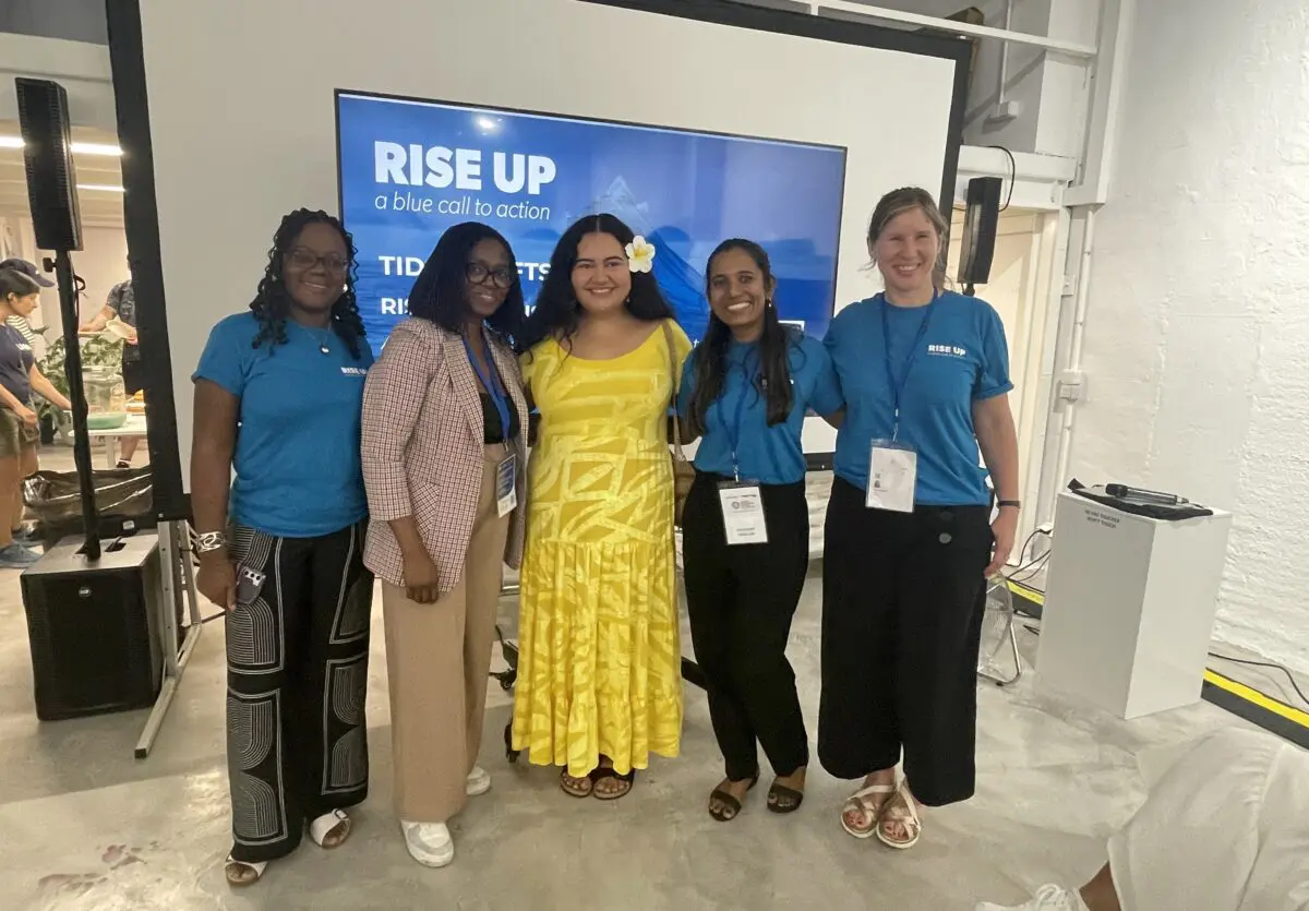 Five people posing in front of a screen reading “RISE UP, a blue call to action”.