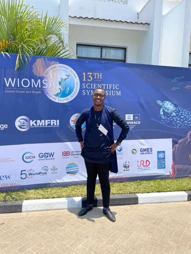Man standing in front of a WIOMSA 13th Scientific Symposium banner.