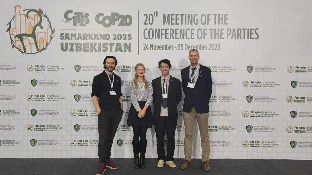 Four people standing in front of a CITES CoP20 conference backdrop
