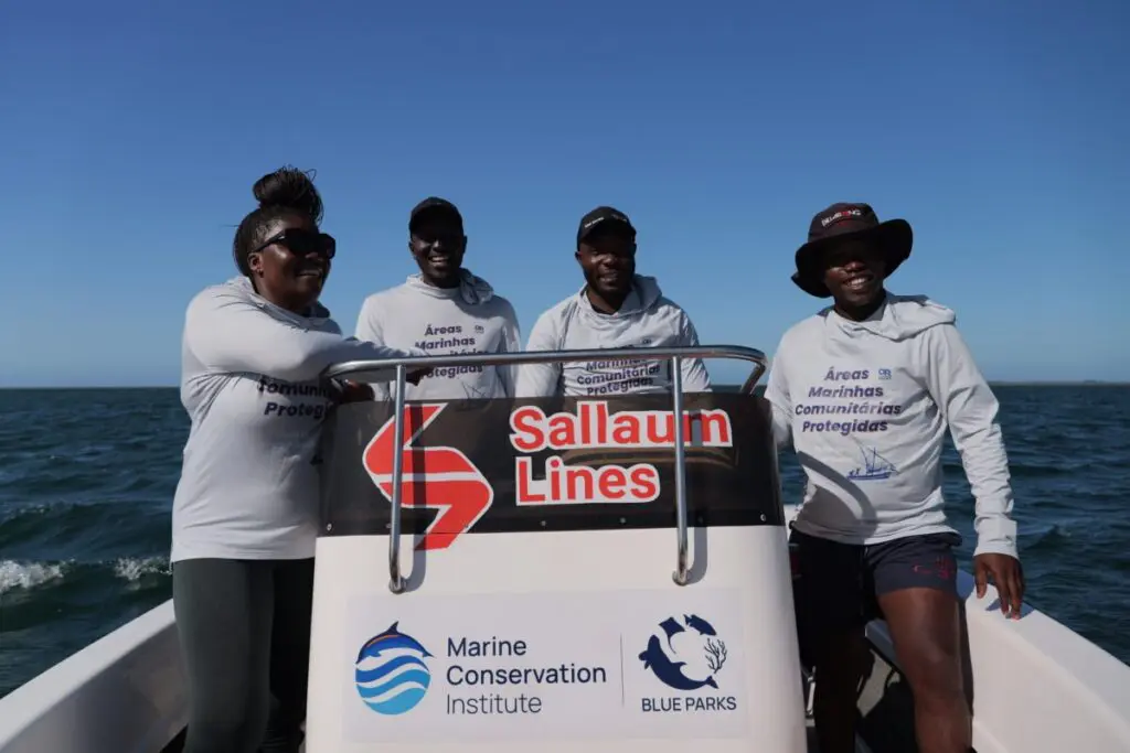 Four people in matching shirts standing on a small boat at sea