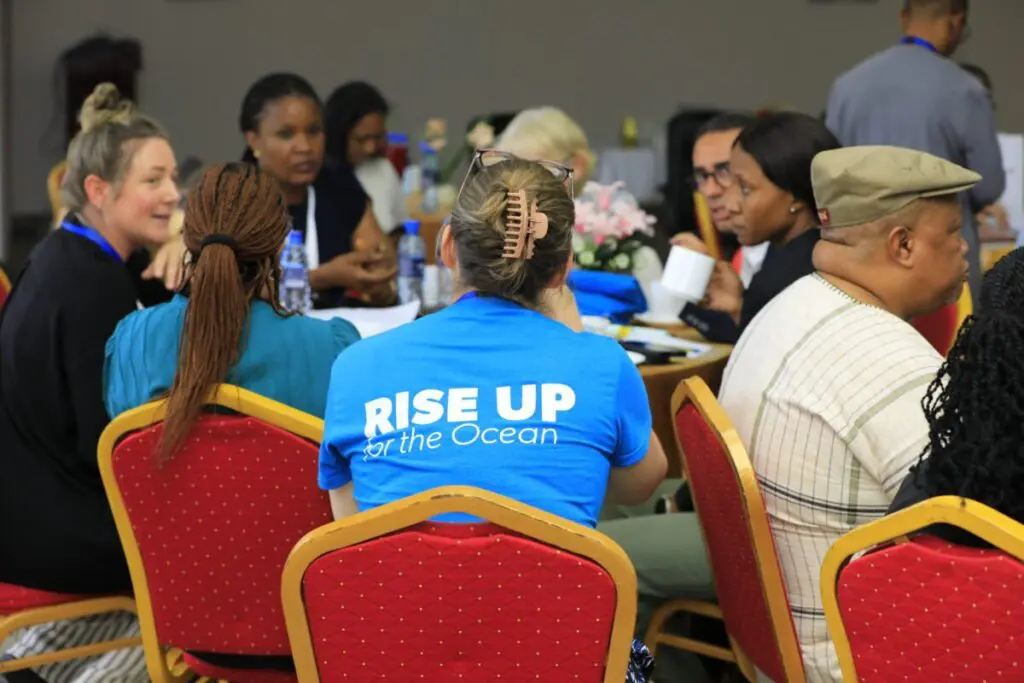 Workshop participants seated around a table, one wearing a RISE UP for the Ocean t-shirt
