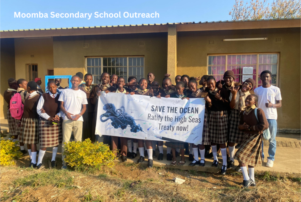 Large group of students and teachers posing outside a school building with a campaign banner