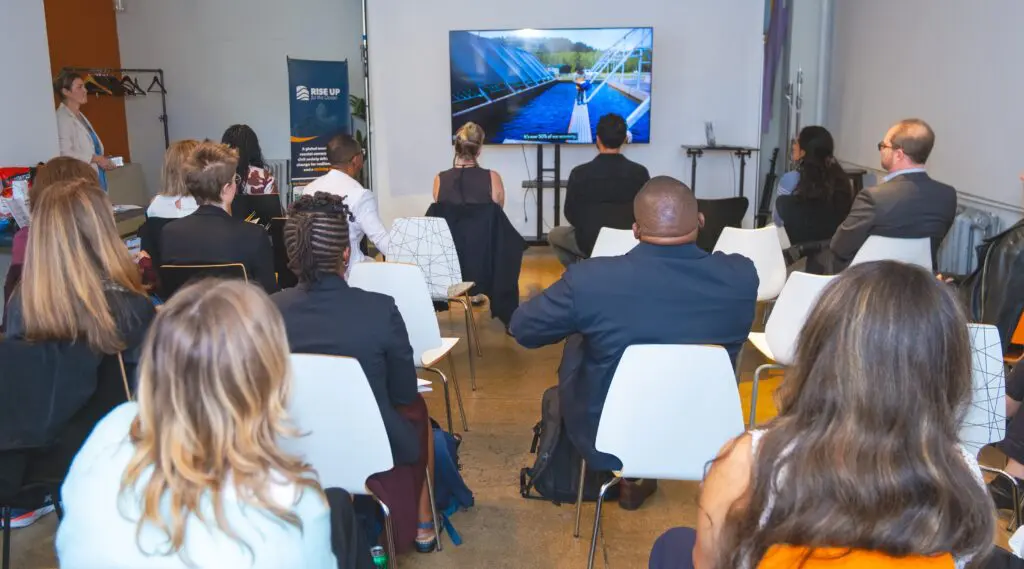Audience seated facing a screen at The Ocean-Climate Nexus event during Climate Week NYC, with a speaker standing beside a RISE UP banner