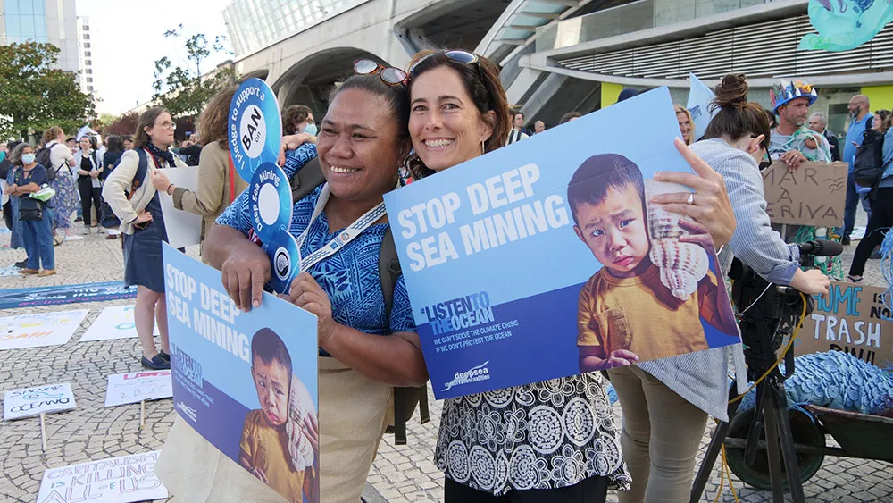Two women holding 'Stop Deep Sea Mining' placards at a demonstration.