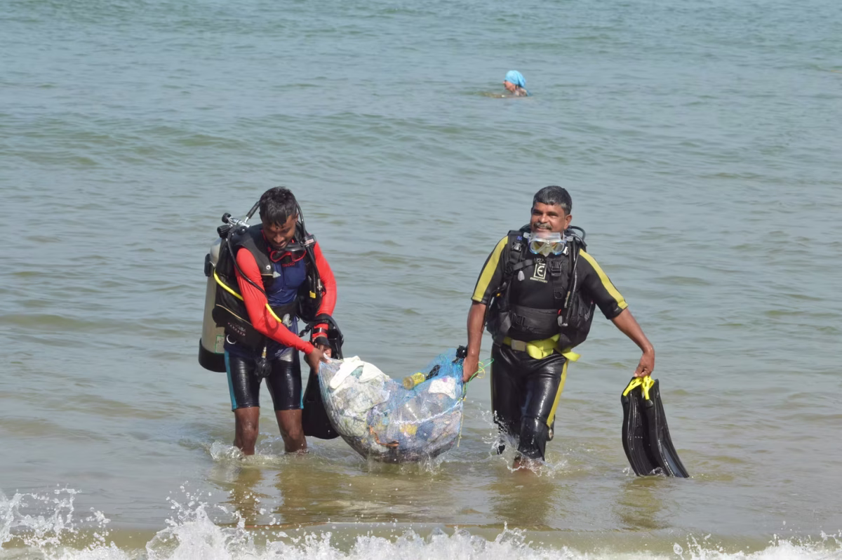 Two scuba divers wading ashore carrying a mesh bag full of collected plastic waste